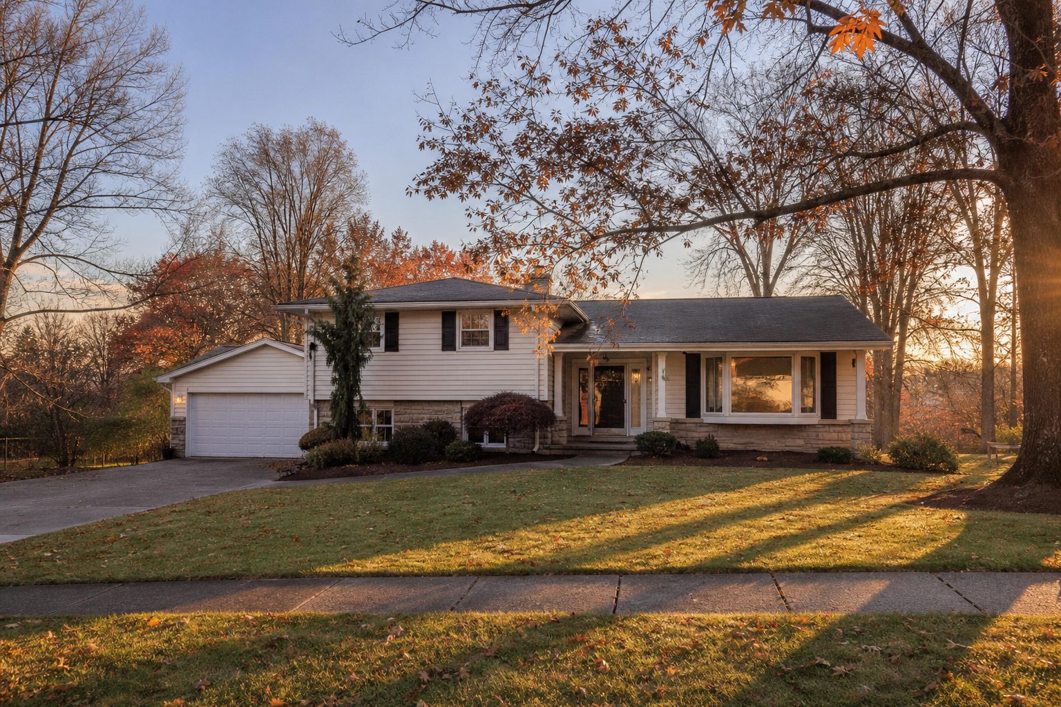 Split-level suburban home in Pittsburgh's North Hills with mature trees and warm evening light casting long lawn shadows.